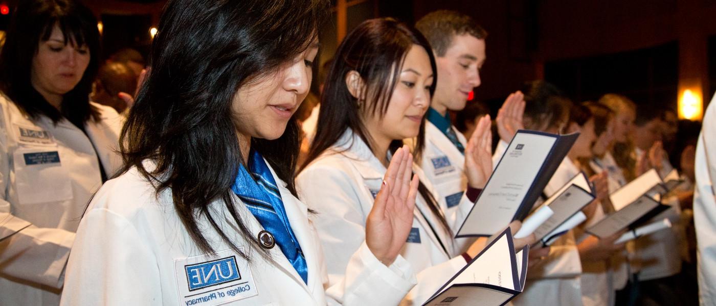 First-year pharmacy students stand in their white coats and recite the pledge of professionalism 
